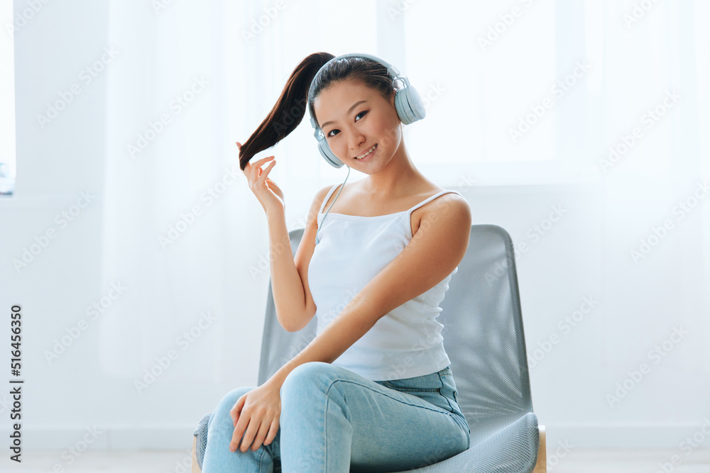 Smiling cheerful tanned lovely young Asian woman in headphones touches hair looks at camera at home interior living room. Sound Studio Stream, Social media concept. Cool offer Banner Wide angle Smiling cheerful tanned lovely young Asian woman in headphones touches hair looks at camera at home interior living room. Sound Studio Stream, Social media concept. Cool offer Banner Wide angle
