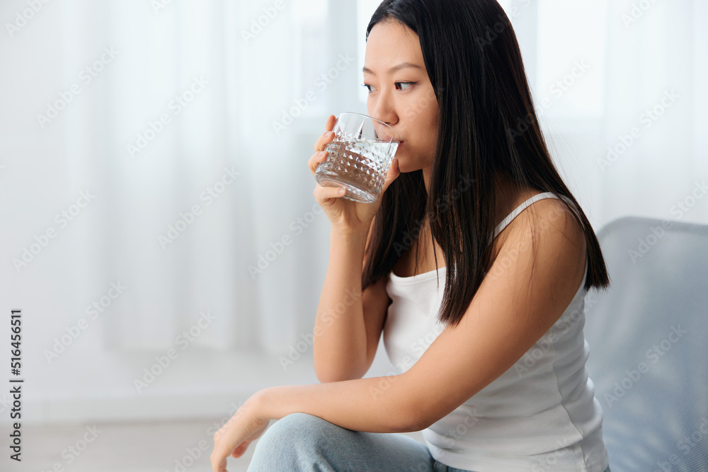 Closeup shot of pensive young Asian cute woman think about bad relationships drink water looks aside sit on chair in light office interior. Breakup from work. Relaxing time concept. Copy space Offer Closeup shot of pensive young Asian cute woman think about bad relationships drink water looks aside sit on chair in light office interior. Breakup from work. Relaxing time concept. Copy space Offer