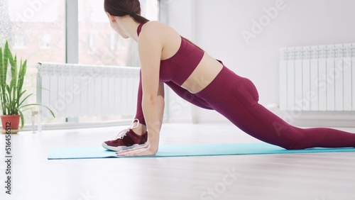 a beautiful and athletic girl in a burgundy tracksuit does gymnastics in the fitness room