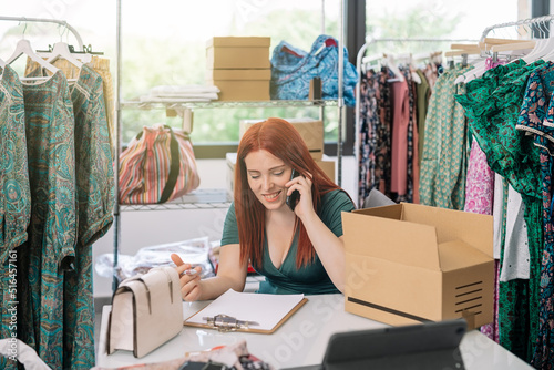 young woman businesswoman smiling, talking on her smartphone with her suppliers and customers in the warehouse of her clothing shop. work and business concept.