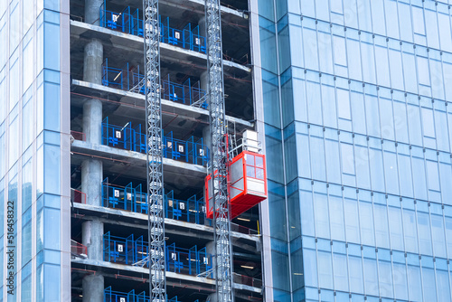 Construction hoist lifting. Erection of high-rise buildings. Red temporary elevator outside the skyscraper. Glass high-riser under construction. Hoist lifting a load at a construction site. photo