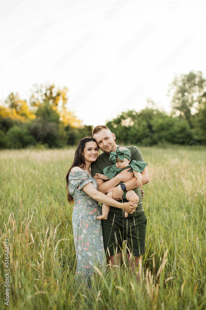 Beautiful caucasian man and woman standing in embrace with their cute little daughter on beautiful summer meadow. Family time on fresh air.