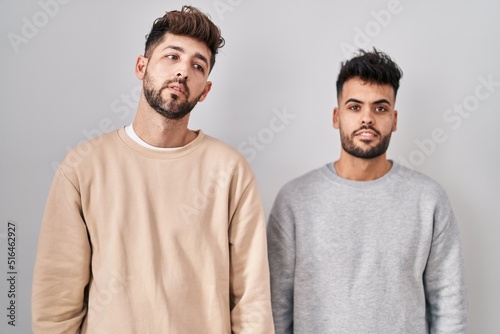 Young homosexual couple standing over white background relaxed with serious expression on face. simple and natural looking at the camera.