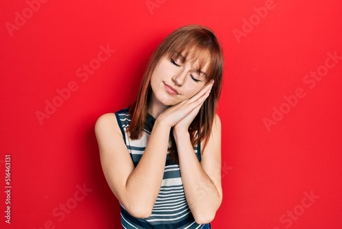 Redhead young woman wearing casual t shirt sleeping tired dreaming and posing with hands together while smiling with closed eyes.