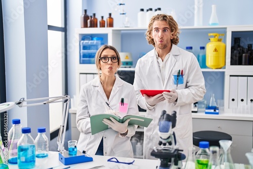 Two people working at scientist laboratory making fish face with mouth and squinting eyes, crazy and comical.