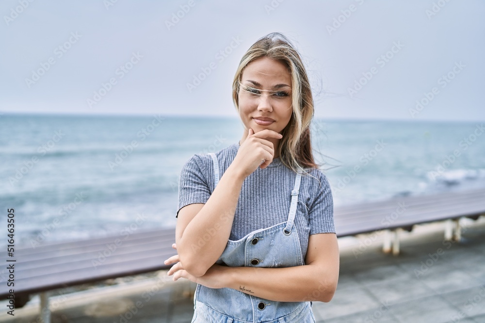 Young caucasian woman outdoors looking confident at the camera with smile with crossed arms and hand raised on chin. thinking positive.