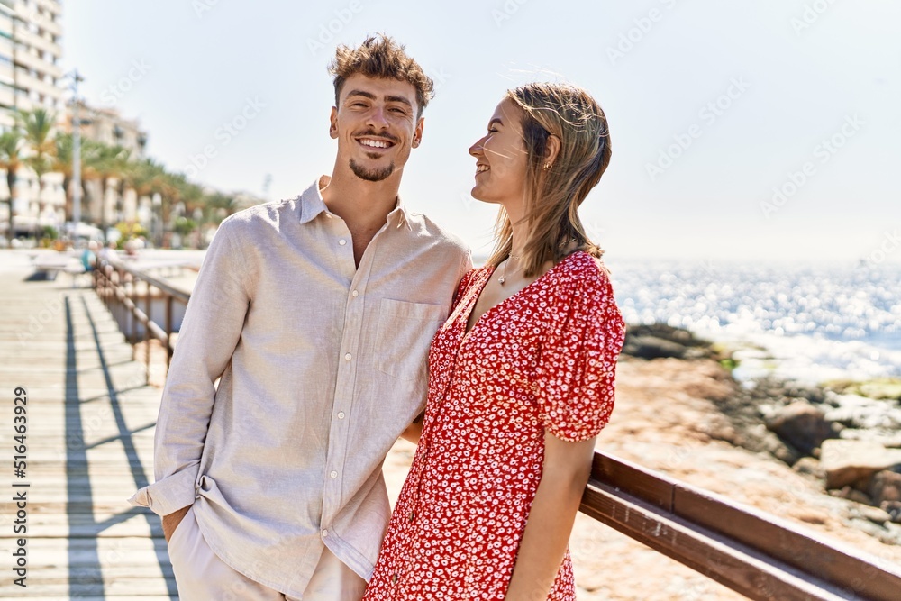 Young hispanic couple on vacation smiling happy and hugging at the beach