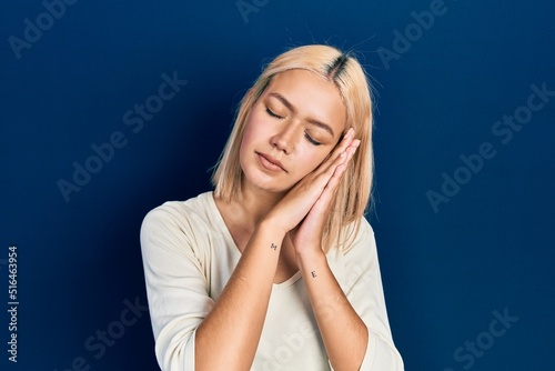 Beautiful blonde woman wearing casual sweater sleeping tired dreaming and posing with hands together while smiling with closed eyes.