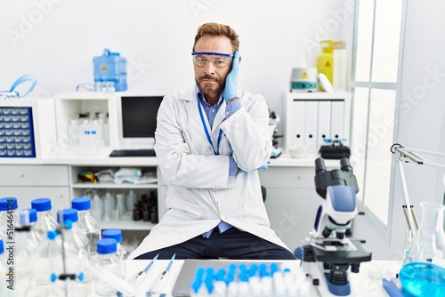 Middle age man working at scientist laboratory thinking looking tired and bored with depression problems with crossed arms.