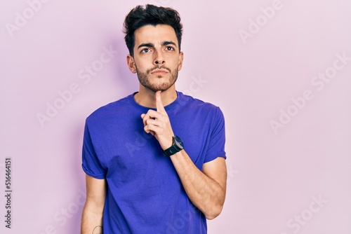 Young hispanic man wearing casual t shirt thinking concentrated about doubt with finger on chin and looking up wondering