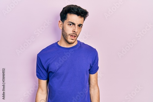 Young hispanic man wearing casual t shirt in shock face, looking skeptical and sarcastic, surprised with open mouth