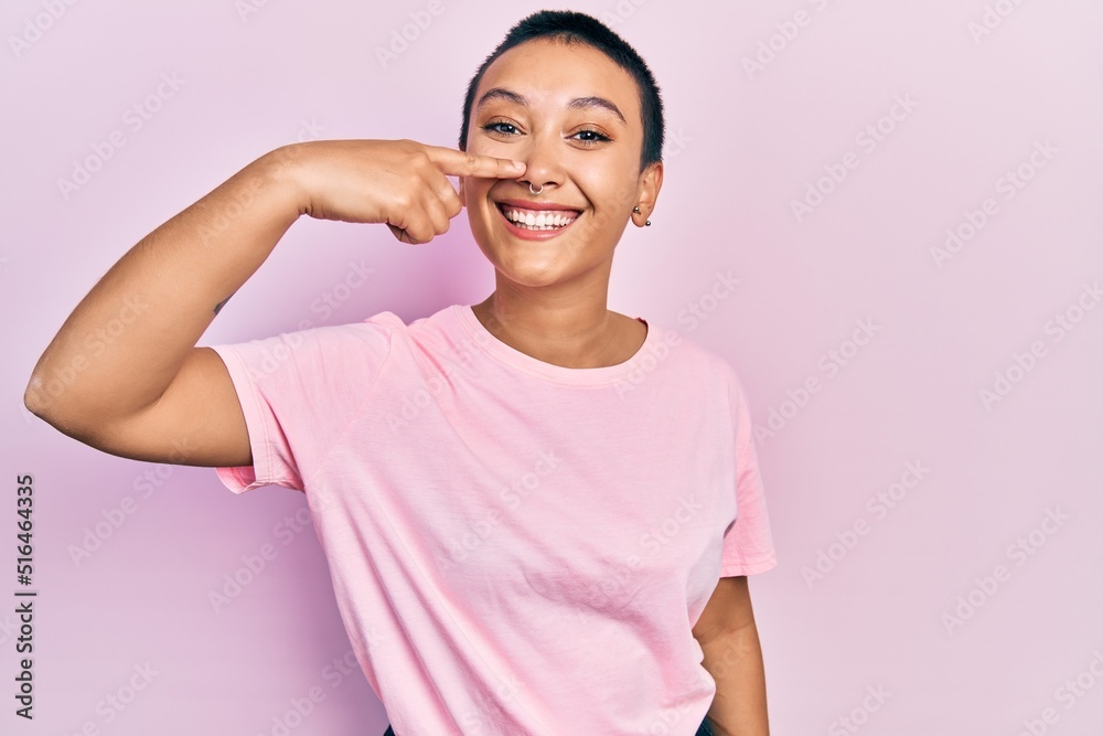 Beautiful hispanic woman with short hair wearing casual pink t shirt pointing with hand finger to face and nose, smiling cheerful. beauty concept Beautiful hispanic woman with short hair wearing casual pink t shirt pointing with hand finger to face and nose, smiling cheerful. beauty concept