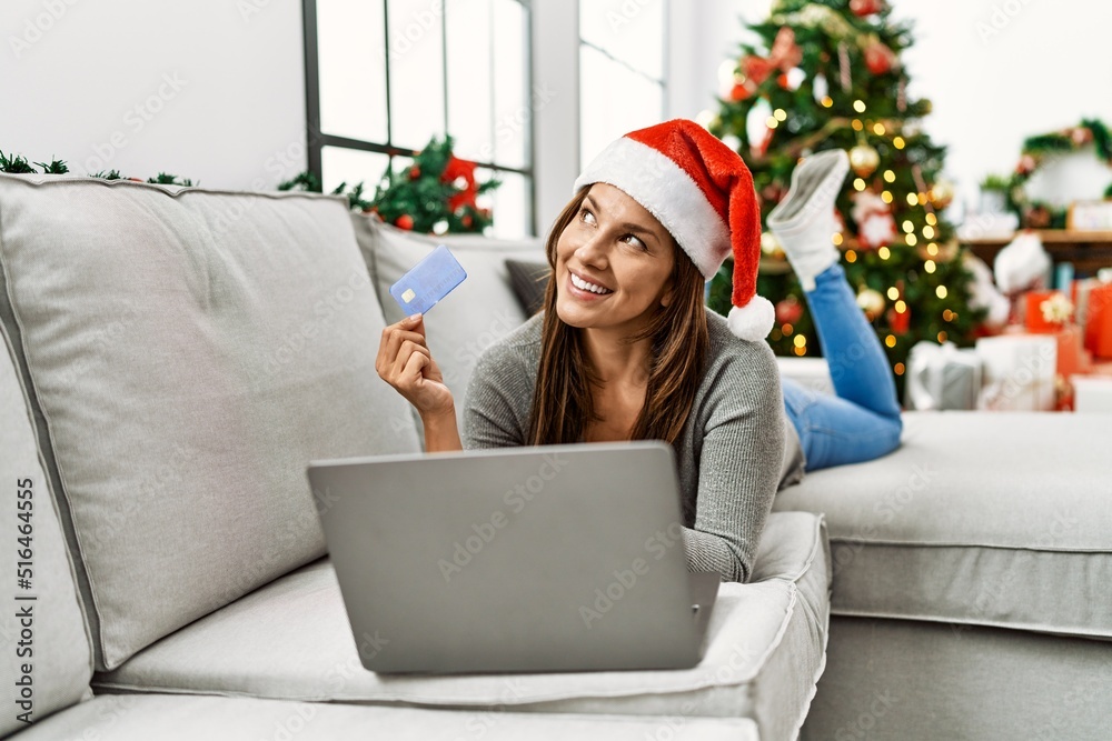 Young latin woman using laptop and credit card lying by christmas tree at home Young latin woman using laptop and credit card lying by christmas tree at home