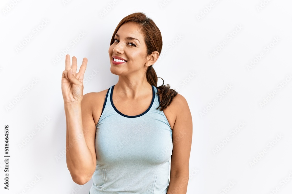 Young latin woman wearing sporty clothes over isolated background showing and pointing up with fingers number three while smiling confident and happy. Young latin woman wearing sporty clothes over isolated background showing and pointing up with fingers number three while smiling confident and happy.