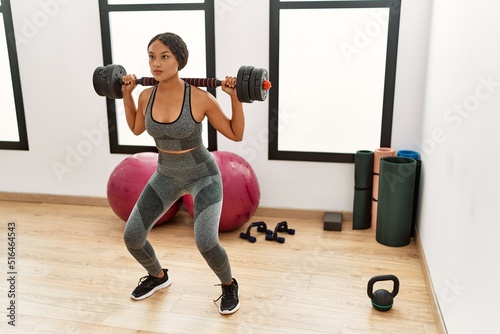 Young latin woman training using dumbbells at sport center