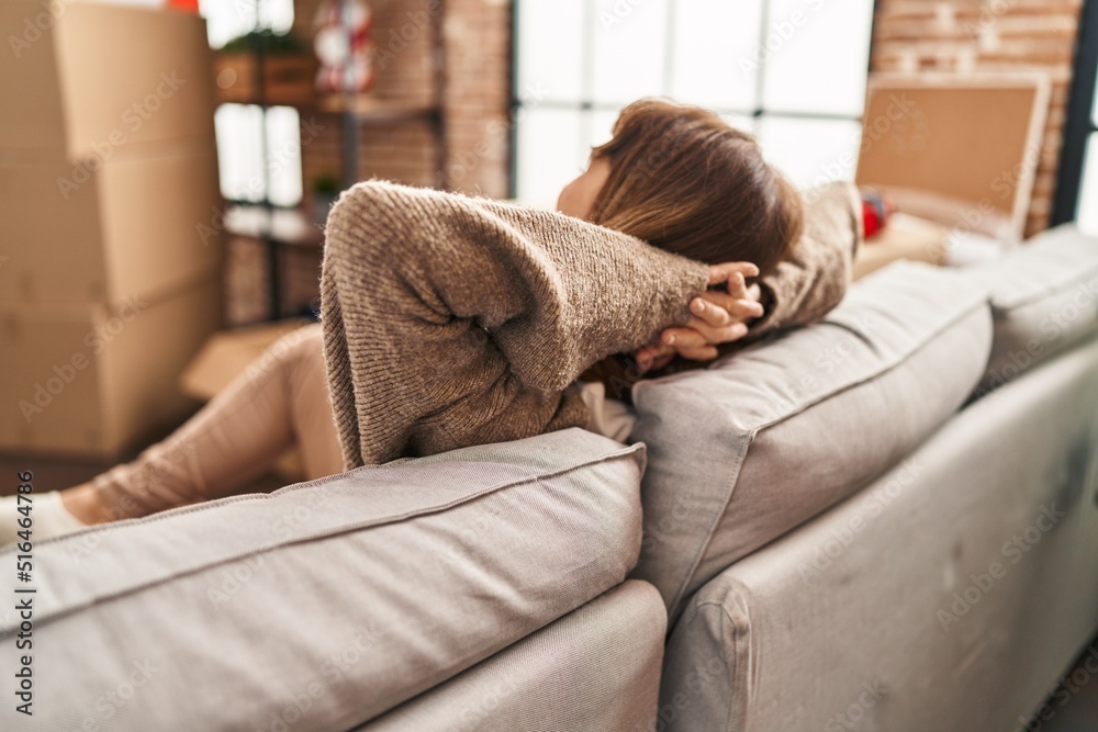 Young caucasian woman relaxed with hands on head sitting on sofa at new home Young caucasian woman relaxed with hands on head sitting on sofa at new home