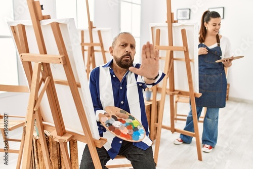 Senior artist man at art studio doing stop sing with palm of the hand. warning expression with negative and serious gesture on the face.