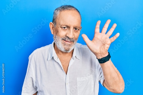 Handsome senior man with beard wearing casual white shirt showing and pointing up with fingers number five while smiling confident and happy.
