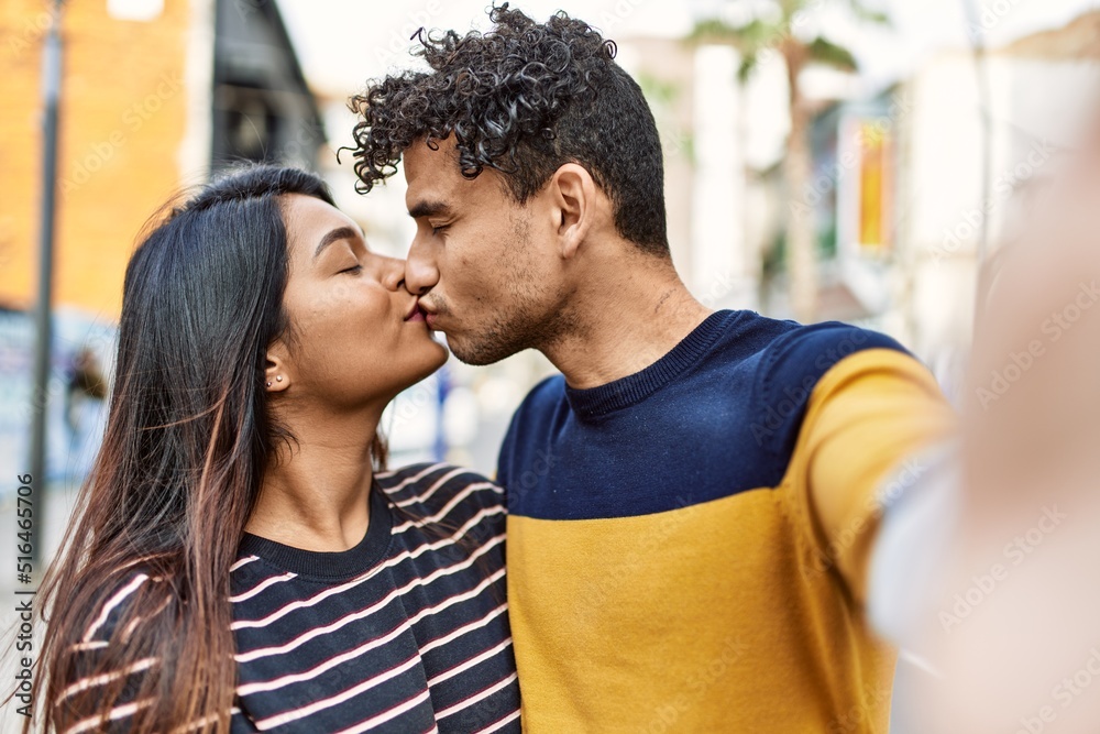 Young latin couple kissing and hugging make selfie by the camera at the city. Young latin couple kissing and hugging make selfie by the camera at the city.