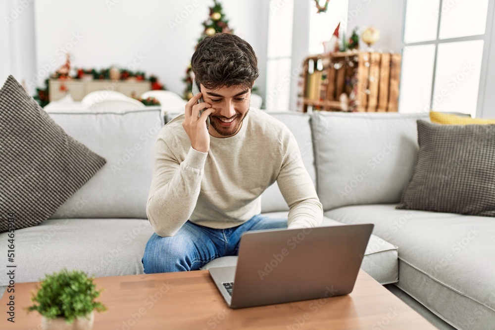 Young hispanic man sitting on the sofa using laptop and smartphone at home. Young hispanic man sitting on the sofa using laptop and smartphone at home.
