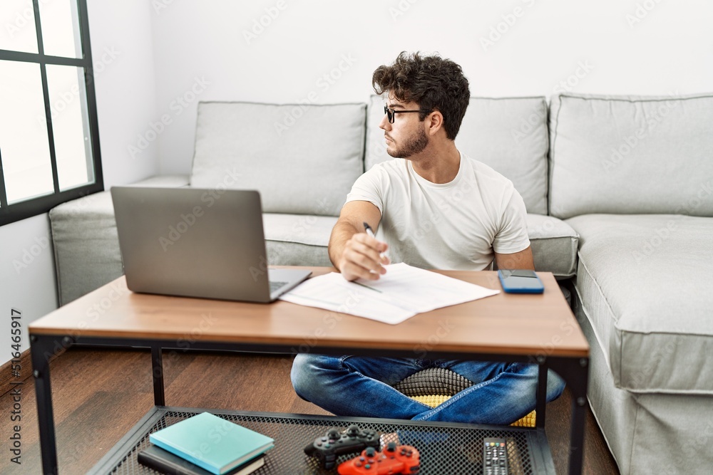 Hispanic man doing papers at home looking to side, relax profile pose with natural face and confident smile.