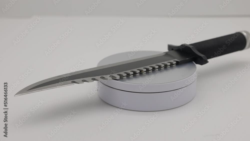Rotating black coated army knife with jagged top edge knife with long blade on white backdrop -close up framing rotating Rotating black coated army knife with jagged top edge knife with long blade on white backdrop -close up framing rotating