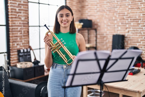 Young hispanic woman musician holding trumpet at music studio