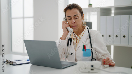 Middle age hispanic woman wearing doctor uniform talking on the telephone at clinic