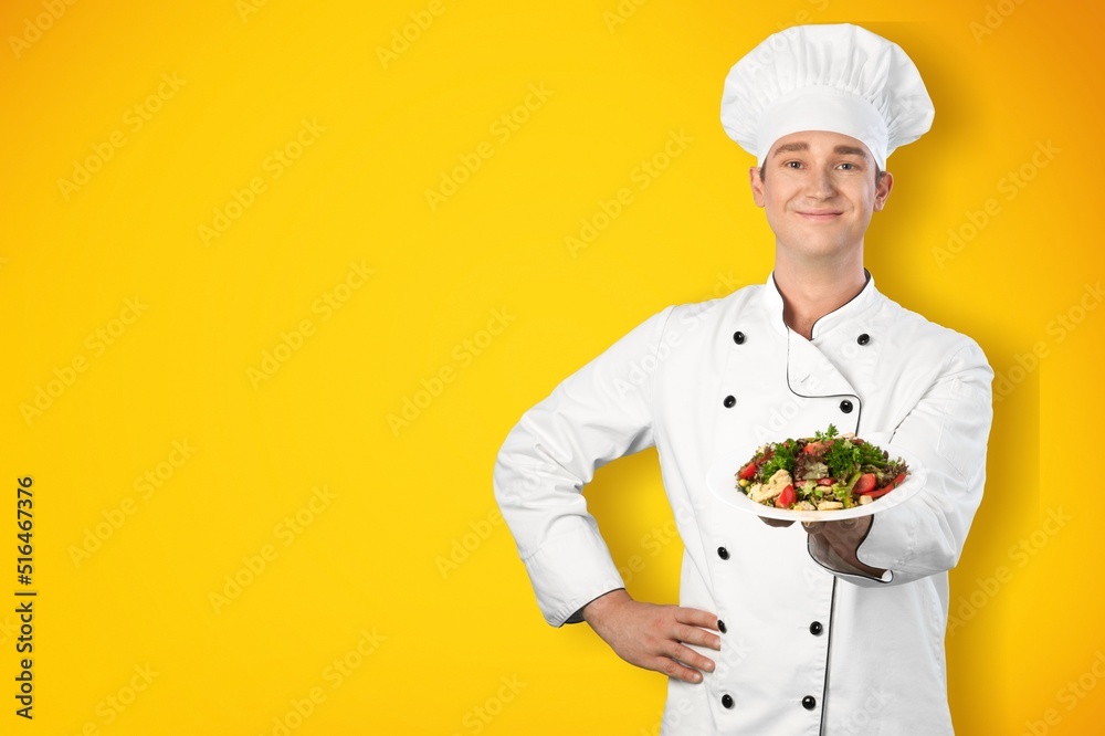 Young man standing and holding plate or dish on yellow background Young man standing and holding plate or dish on yellow background