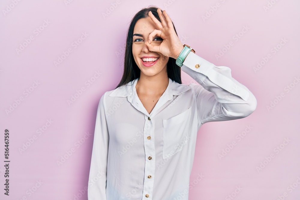 Beautiful woman with blue eyes wearing casual white shirt smiling happy doing ok sign with hand on eye looking through fingers Beautiful woman with blue eyes wearing casual white shirt smiling happy doing ok sign with hand on eye looking through fingers