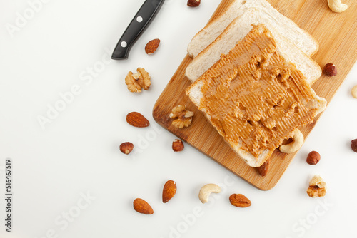 Square bread for toast with peanut butter on a wooden board. Nuts, a knife and a wooden cutting board with a sandwich and slices of bread on a white table.