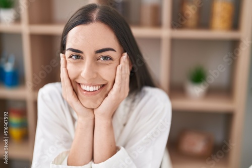 Young hispanic woman smiling confident sitting on table at home
