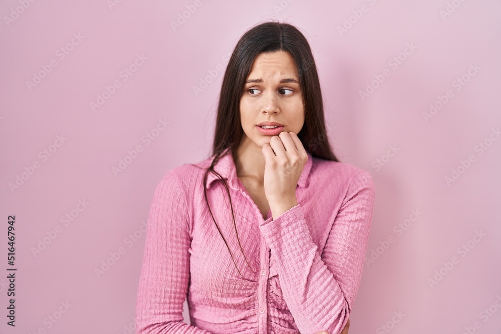 Young hispanic woman standing over pink background looking stressed and nervous with hands on mouth biting nails. anxiety problem. Young hispanic woman standing over pink background looking stressed and nervous with hands on mouth biting nails. anxiety problem.