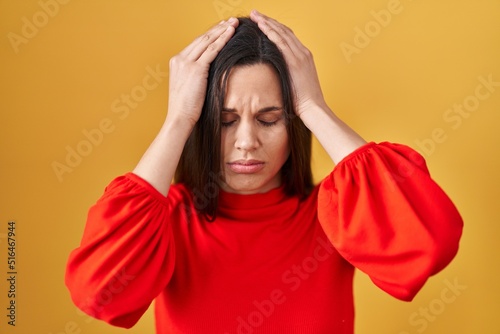 Young hispanic woman standing over yellow background suffering from headache desperate and stressed because pain and migraine. hands on head.