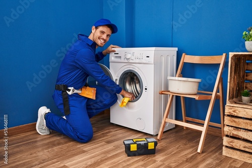 Young hispanic man technician cleaning washing machine at laundry room