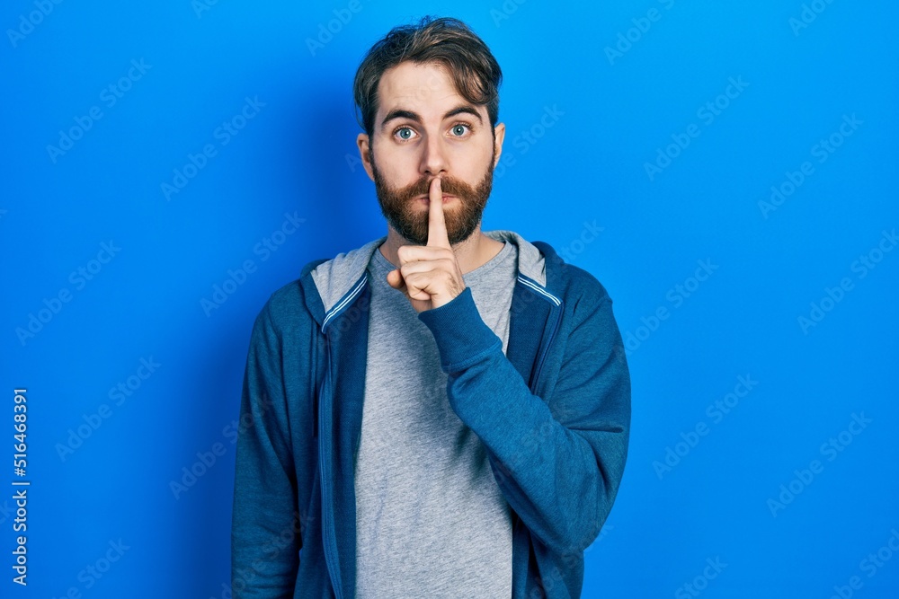 Caucasian man with beard wearing casual sweatshirt asking to be quiet with finger on lips. silence and secret concept. Caucasian man with beard wearing casual sweatshirt asking to be quiet with finger on lips. silence and secret concept.