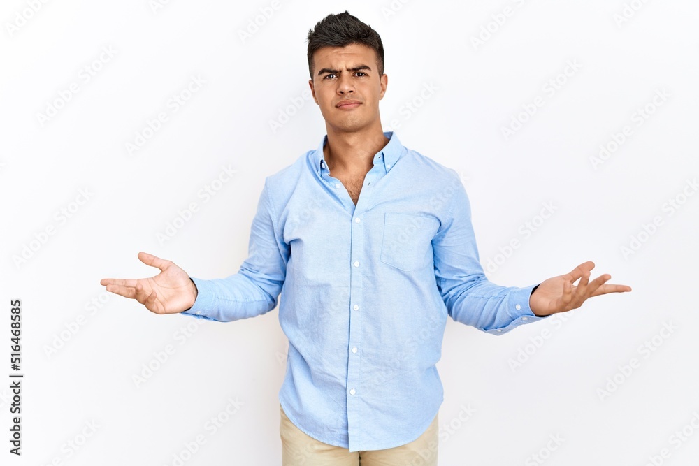 Young hispanic man wearing business shirt standing over isolated background clueless and confused with open arms, no idea concept. Young hispanic man wearing business shirt standing over isolated background clueless and confused with open arms, no idea concept.