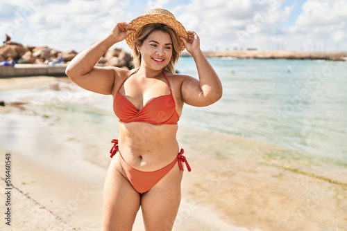 Young hispanic woman wearing bikini and summer hat standing at seaside