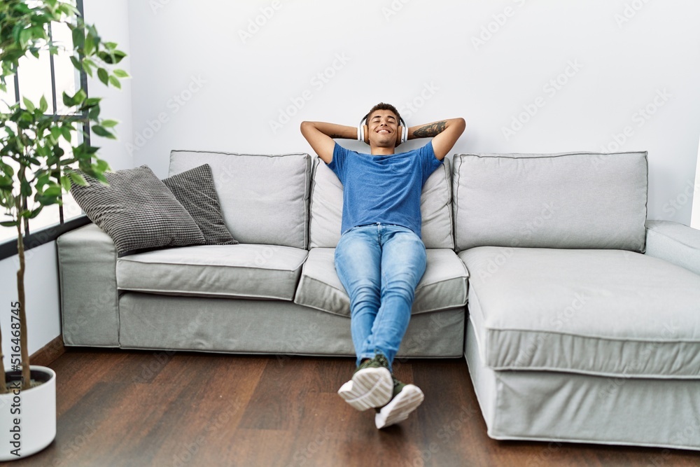 Young hispanic man relaxing sitting on the sofa wearing headphones at home
