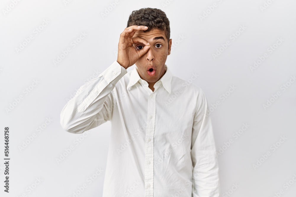 Young handsome hispanic man standing over isolated background doing ok gesture shocked with surprised face, eye looking through fingers. unbelieving expression. Young handsome hispanic man standing over isolated background doing ok gesture shocked with surprised face, eye looking through fingers. unbelieving expression.