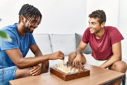 Two men friends playing chess sitting on sofa at home