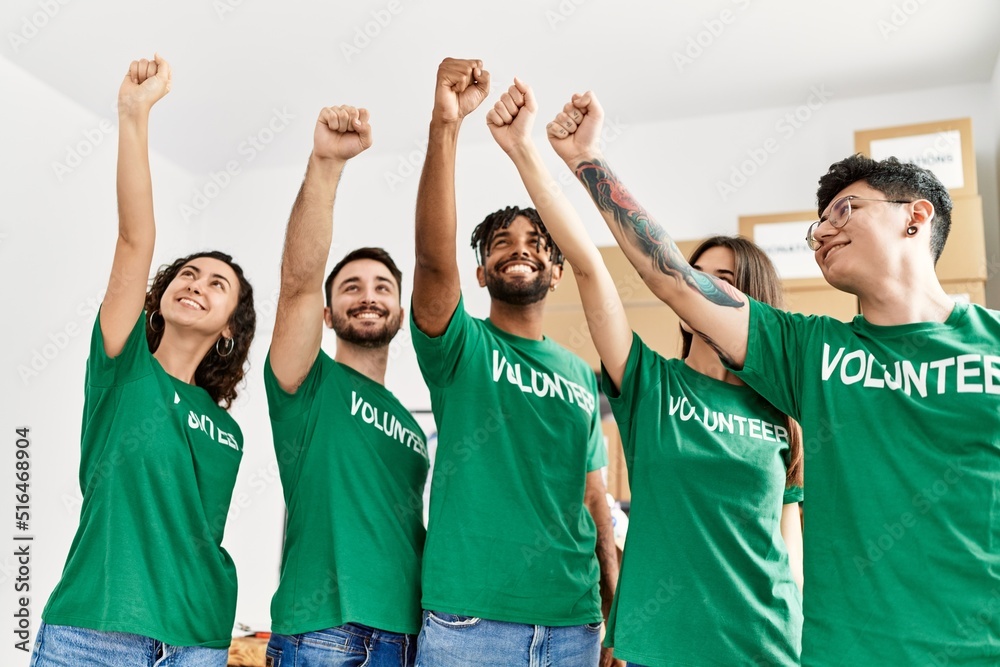 Fototapeta premium Group of young volunteers smiling happy with fists raised up at charity center.