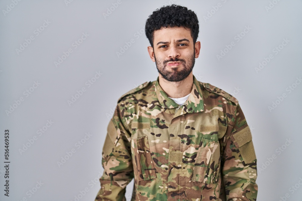 Arab man wearing camouflage army uniform puffing cheeks with funny face. mouth inflated with air, crazy expression.