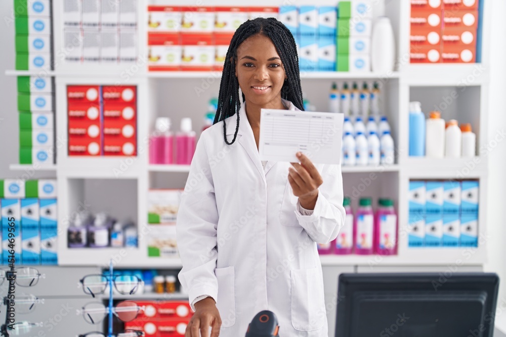 African american woman pharmacist smiling confident holding prescription at pharmacy