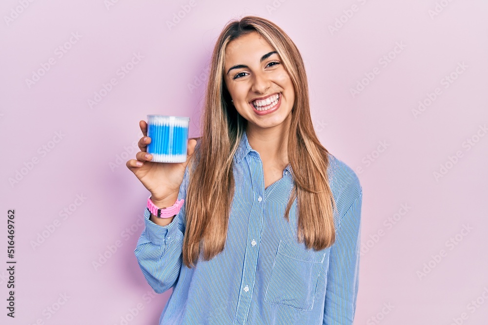 Beautiful hispanic woman holding earwax cotton removers looking positive and happy standing and smiling with a confident smile showing teeth Beautiful hispanic woman holding earwax cotton removers looking positive and happy standing and smiling with a confident smile showing teeth