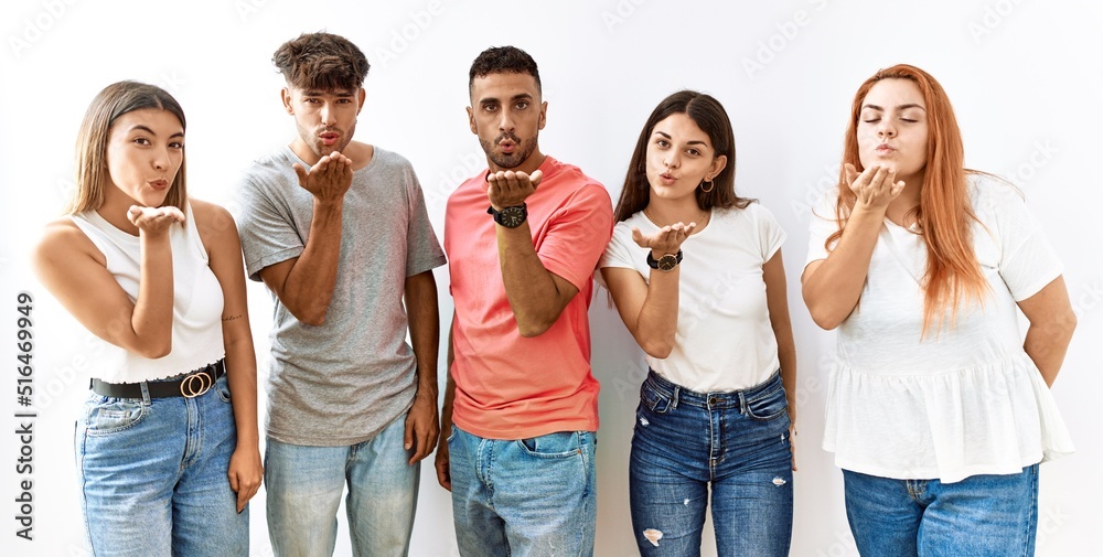 Group of young friends standing together over isolated background looking at the camera blowing a kiss with hand on air being lovely and sexy. love expression. Group of young friends standing together over isolated background looking at the camera blowing a kiss with hand on air being lovely and sexy. love expression.