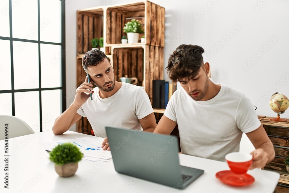 Two hispanic men couple talking on the smartphone and using laptop working at home Two hispanic men couple talking on the smartphone and using laptop working at home