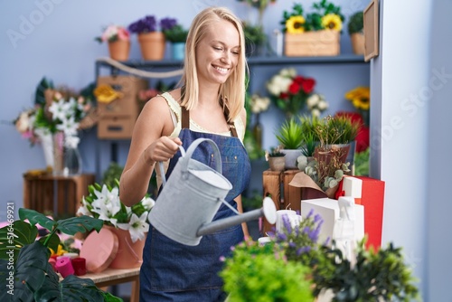 Young blonde woman florist smiling confident watering plant at florist store