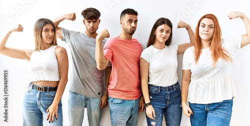 Group of young friends standing together over isolated background strong person showing arm muscle  confident and proud of power