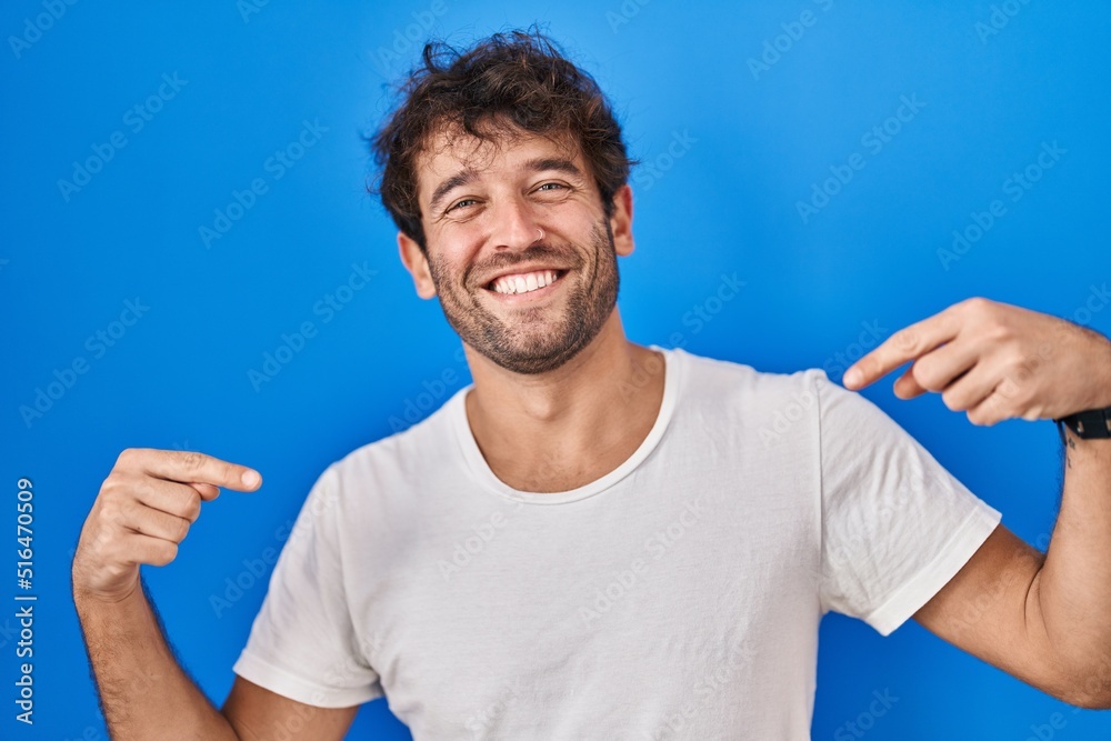 Hispanic young man standing over blue background looking confident with smile on face, pointing oneself with fingers proud and happy. Hispanic young man standing over blue background looking confident with smile on face, pointing oneself with fingers proud and happy.
